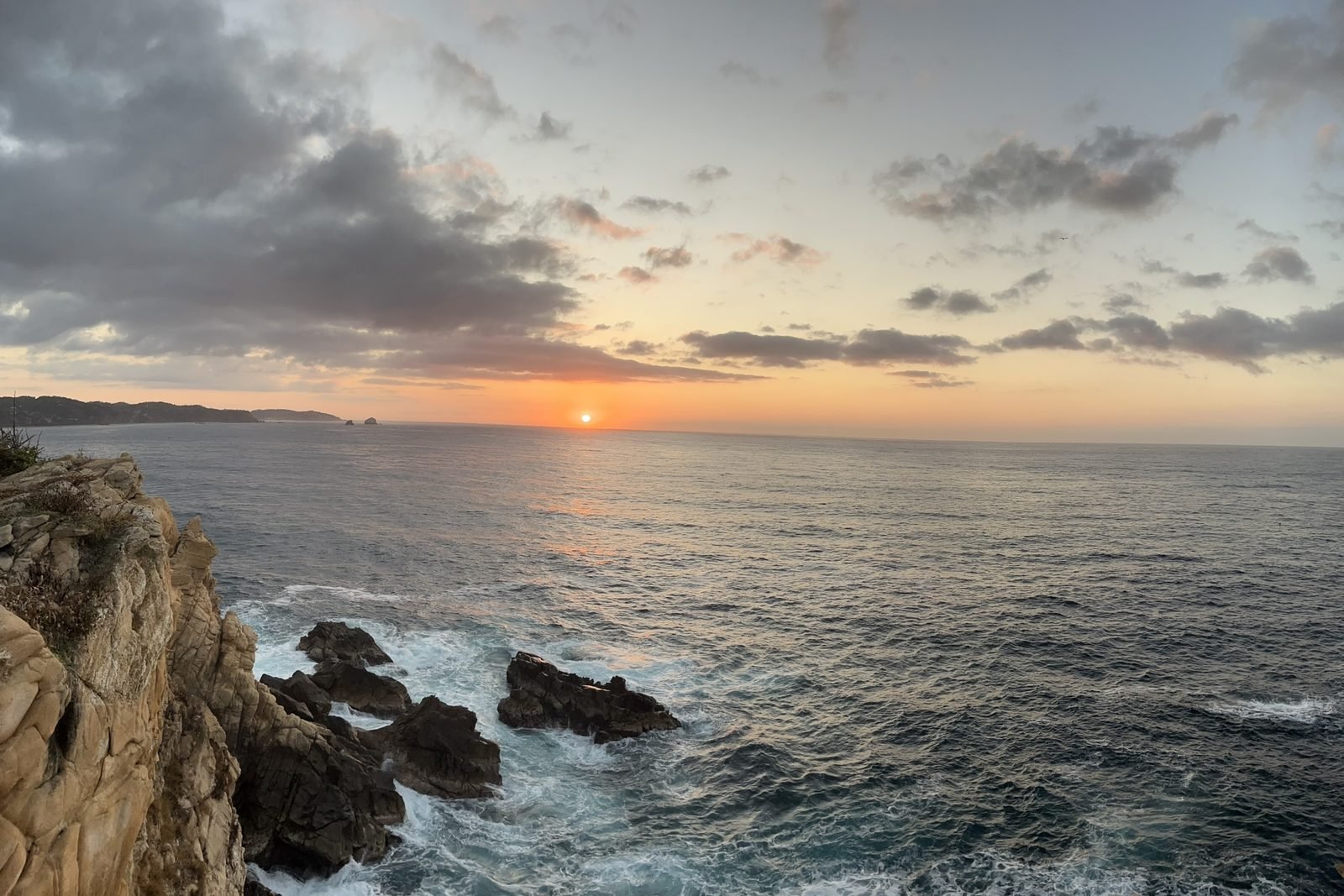 Atardecer dorado sobre el Pacífico desde Punta Cometa, con el sol tocando el horizonte y las rocas del acantilado
